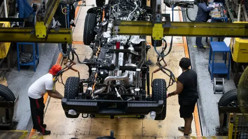 عمال في مصنع لتجميع السيارات يقومون بتركيب أجزاء على هيكل سيارة، مما يعكس تأثير الرسوم الجمركية على أسعار السيارات في أمريكا الشمالية.