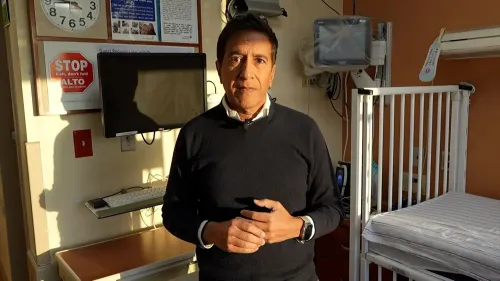 طبيب يتحدث عن تفشي الحصبة في تكساس، مع وجود سرير طفل خلفه وشاشة عرض، في سياق التحذيرات الصحية.