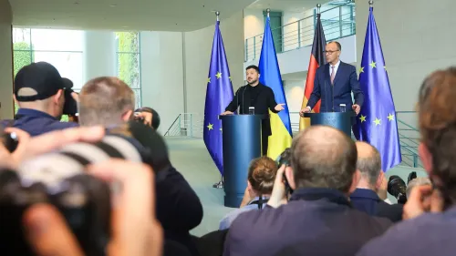 زيلينسكي وميرتس يتحدثان خلال مؤتمر صحفي في برلين، مع أعلام أوكرانيا وألمانيا والاتحاد الأوروبي خلفهما، وسط حشد من الصحفيين.