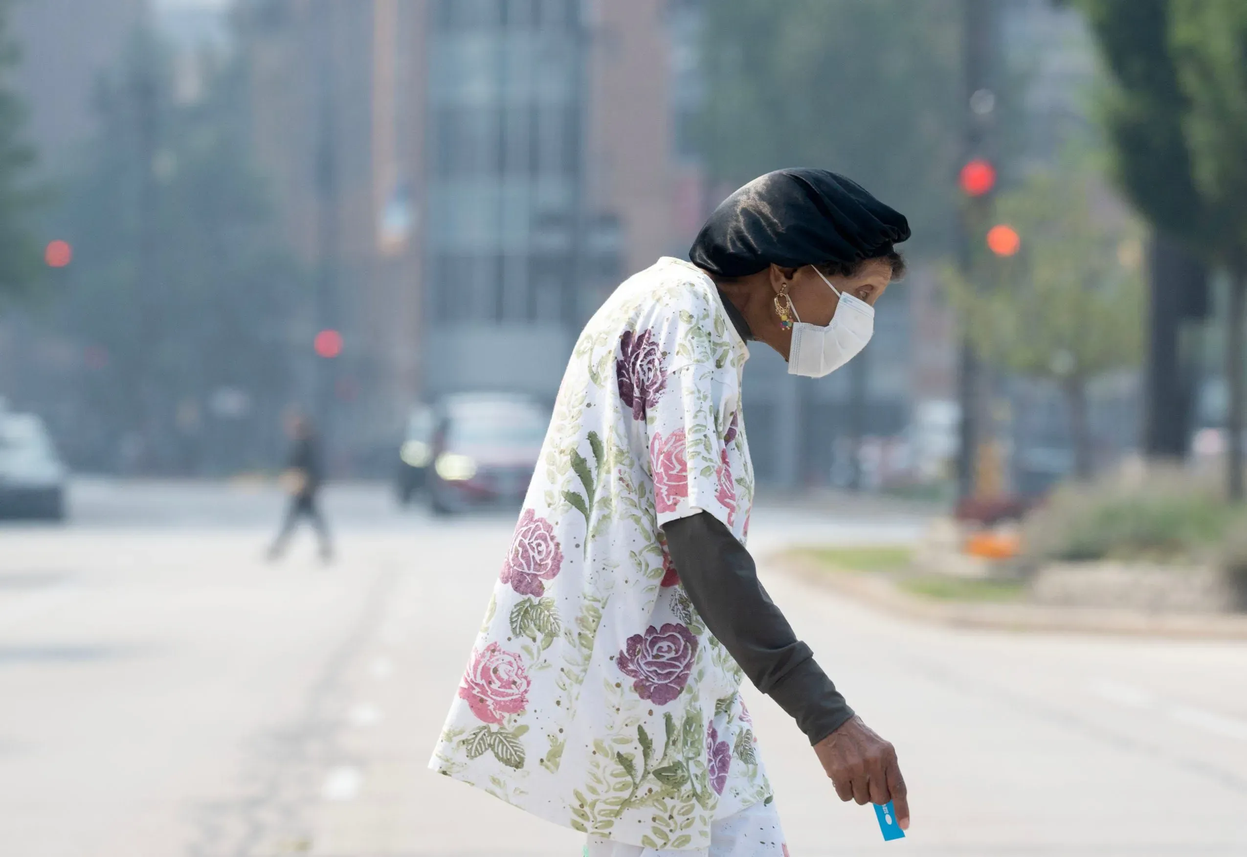 امرأة ترتدي كمامة وتسير في شارع ملبد بالدخان، مما يعكس تأثير حرائق الغابات الكندية على جودة الهواء في الولايات المتحدة.