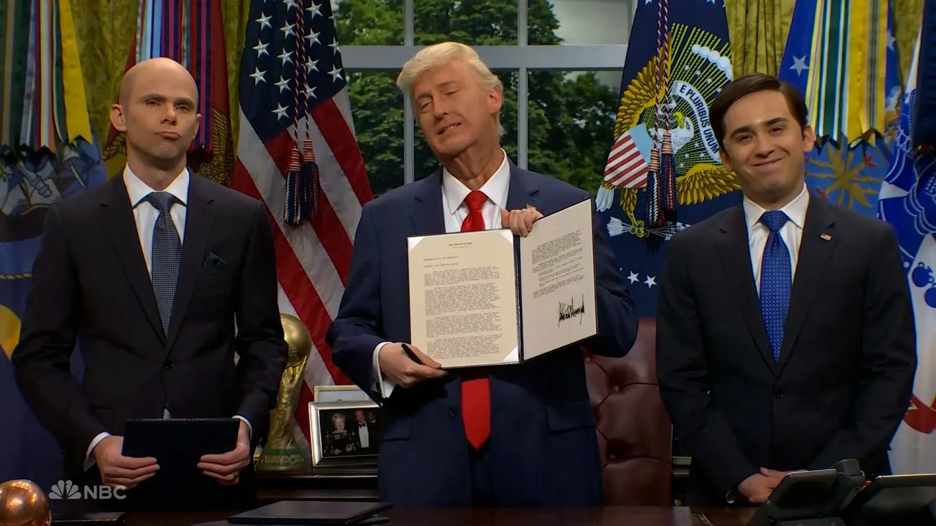 جيمس أوستن جونسون يجسد شخصية ترامب في المكتب البيضاوي، ممسكًا بأمر تنفيذي، بينما يقف مايكي داي في دور ستيفن ميلر.