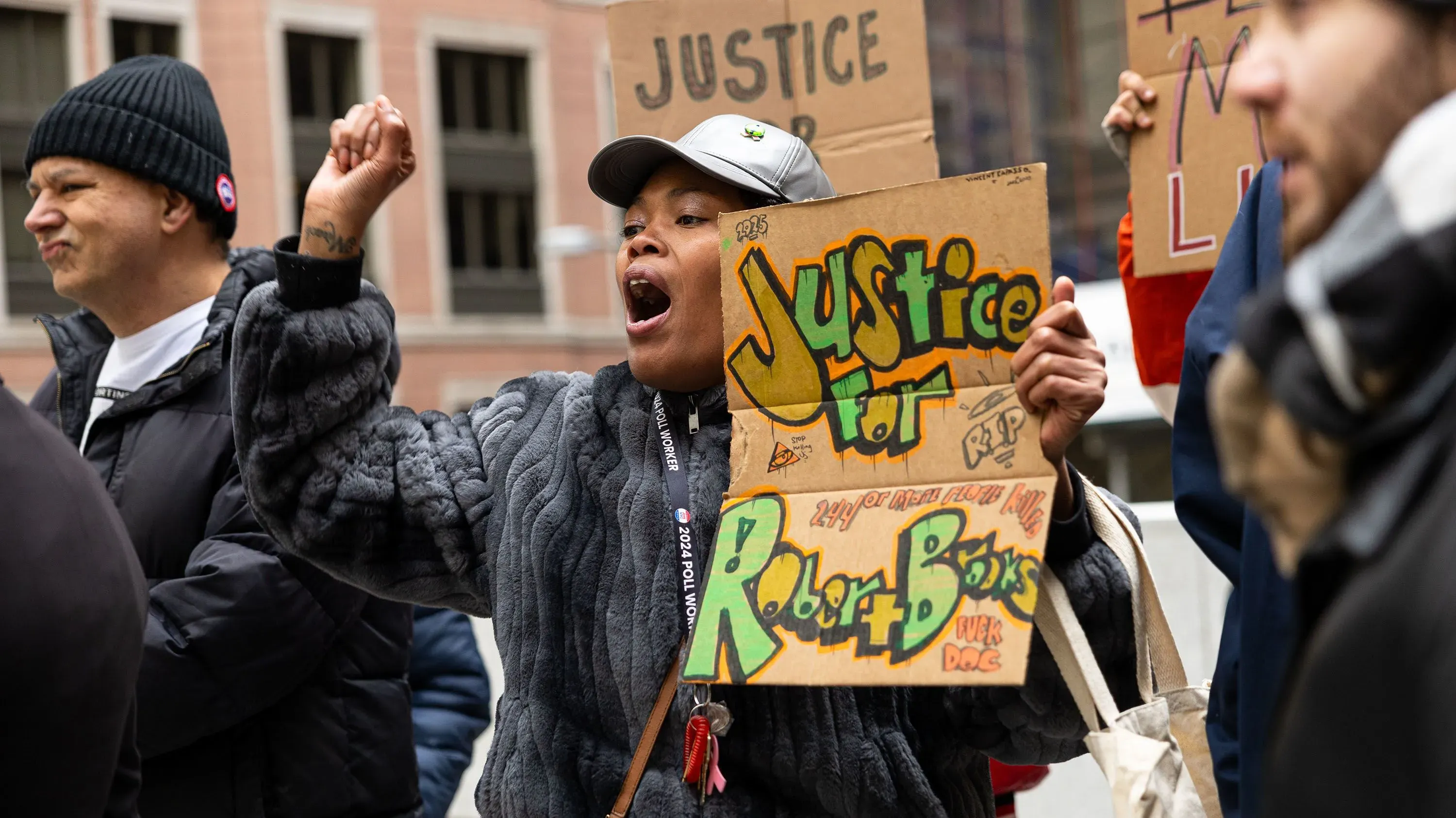 محتجّة تحمل لافتة تطالب بالعدالة لروبرت بروكس، مع تعبير عن الغضب في مظاهرة ضد العنف في السجون.