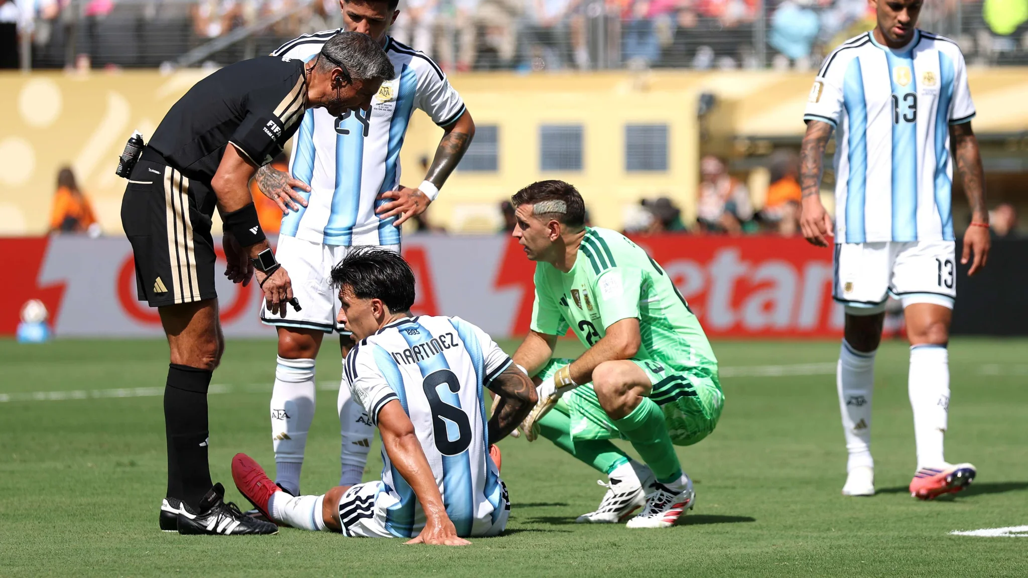 لاعبو منتخب الأرجنتين يتلقون العلاج على أرض الملعب خلال مباراة كأس العالم، مع حكم يتحدث إلى لاعب جالس يعاني من إصابة وسط أجواء توتر المباراة.