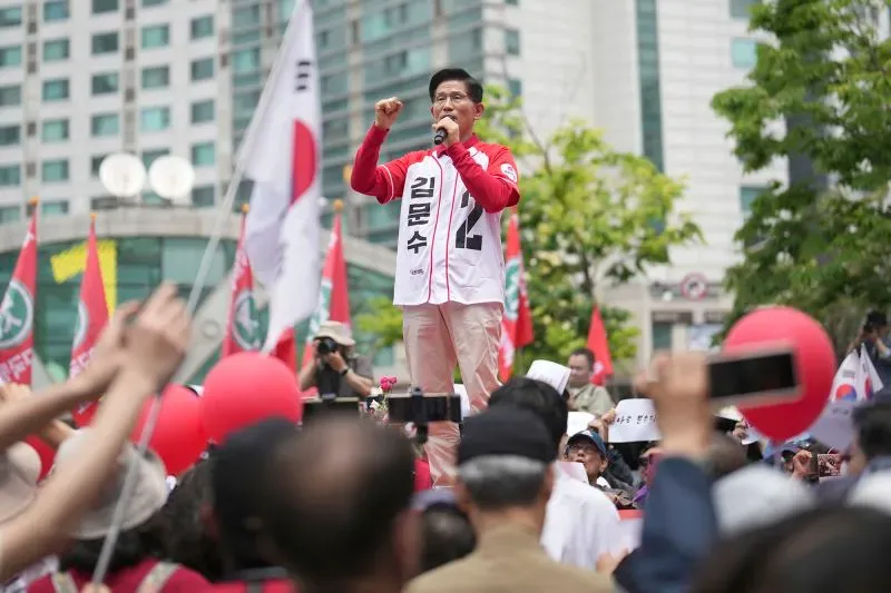 كيم مون سو، المرشح الرئاسي من حزب سلطة الشعب، يتحدث في تجمع حاشد، مع أعلام حمراء وأعداد كبيرة من المؤيدين في الخلفية.