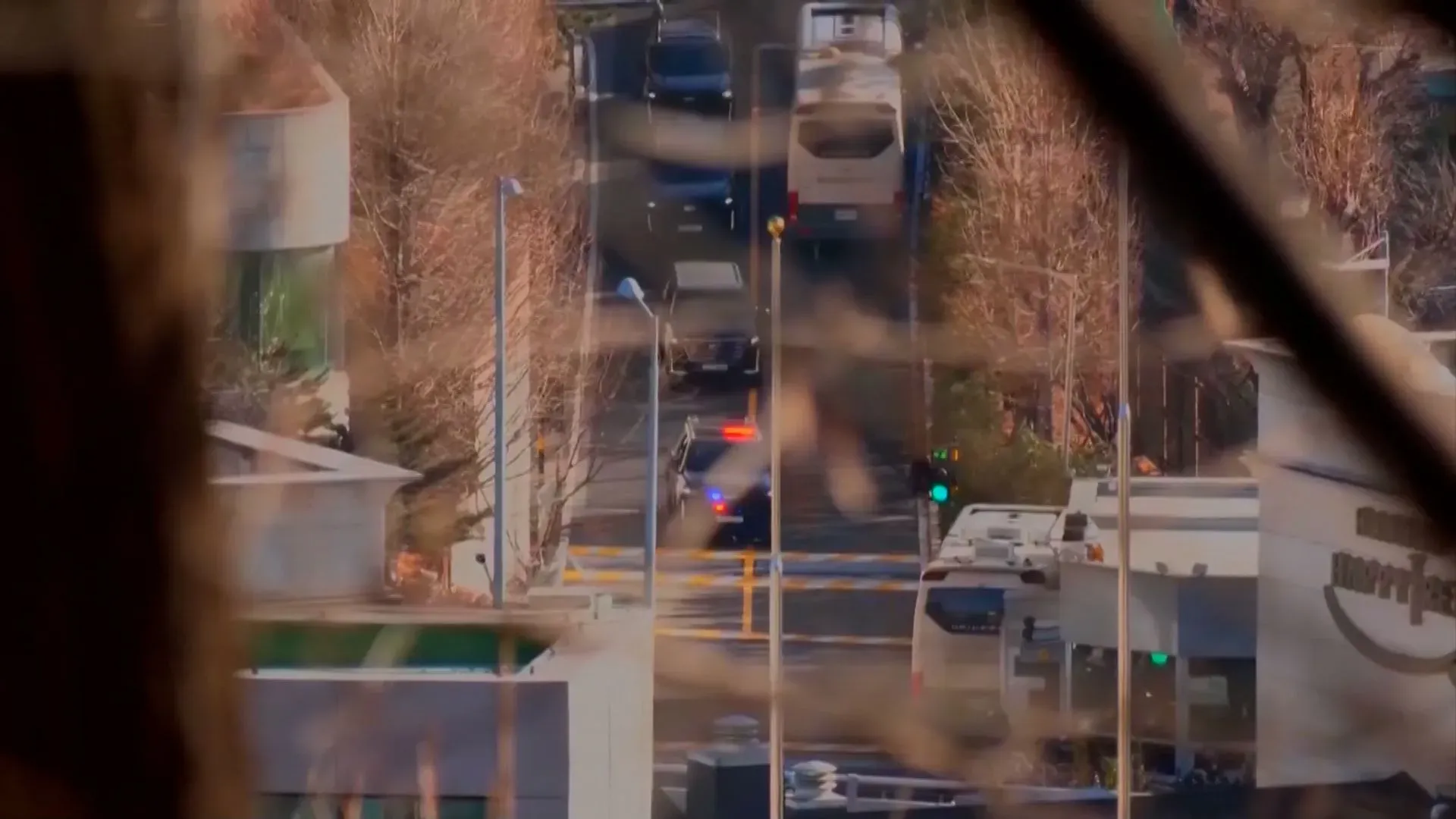 مشهد لسيارات الشرطة والمركبات الأخرى تتجه نحو مركز احتجاز الرئيس الكوري الجنوبي المعزول يون سوك يول، مع وجود أشجار في الخلفية.