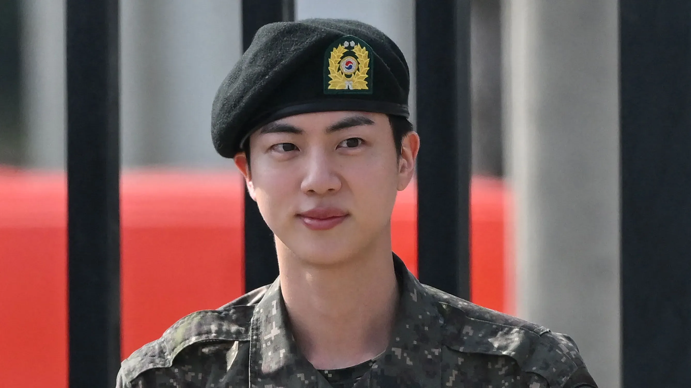جين، عضو فرقة BTS، يرتدي زيًا عسكريًا وقبعة، ويظهر في حدث بعد انتهاء خدمته العسكرية في سيول، محاطًا بجو احتفالي.