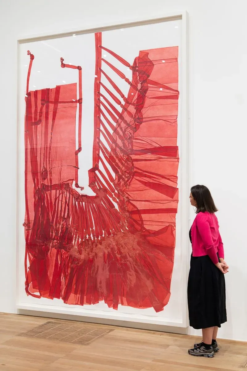 عمل فني لجدارية حمراء معقدة، تعرض تفاصيل هندسية، بينما تتأمل زائرة المعرض في معرض تيت مودرن بلندن.