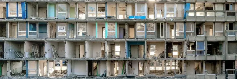 واجهة مبنى مدمرة تظهر فتحات نوافذ وأبواب، تعكس حالة التحول والتهدم، مما يبرز موضوع الذاكرة والهوية في الفن المعاصر.