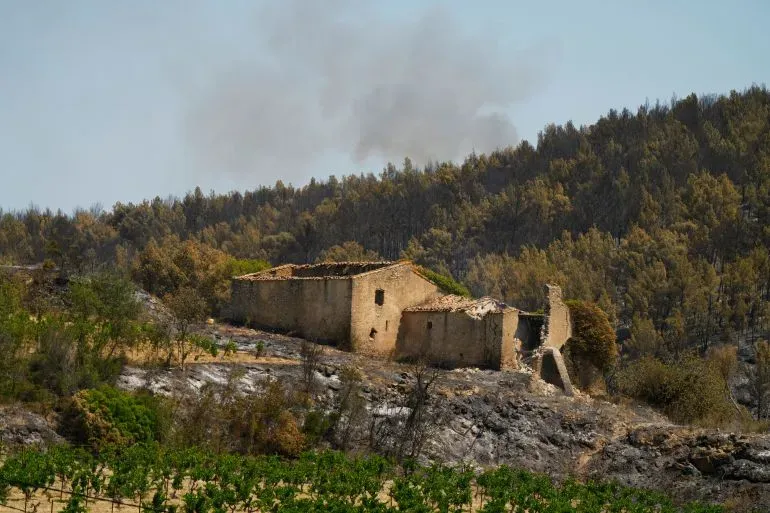 دخان يتصاعد من منطقة حريق في جنوب فرنسا، حيث تظهر بقايا منزل محترق وسط غابة دمرتها النيران، مما يعكس تأثير موجة الحر.