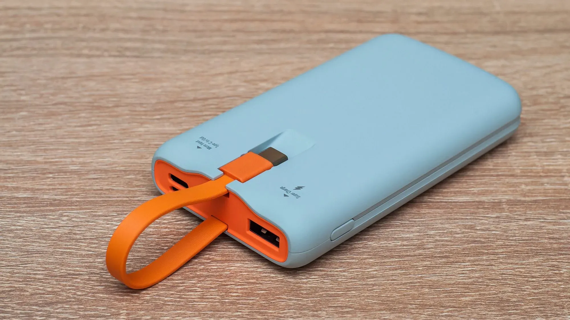 بنك طاقة محمول باللون الأزرق مع حزام برتقالي، موضوع على سطح خشبي، يشير إلى أهمية السلامة أثناء السفر بالطائرة.