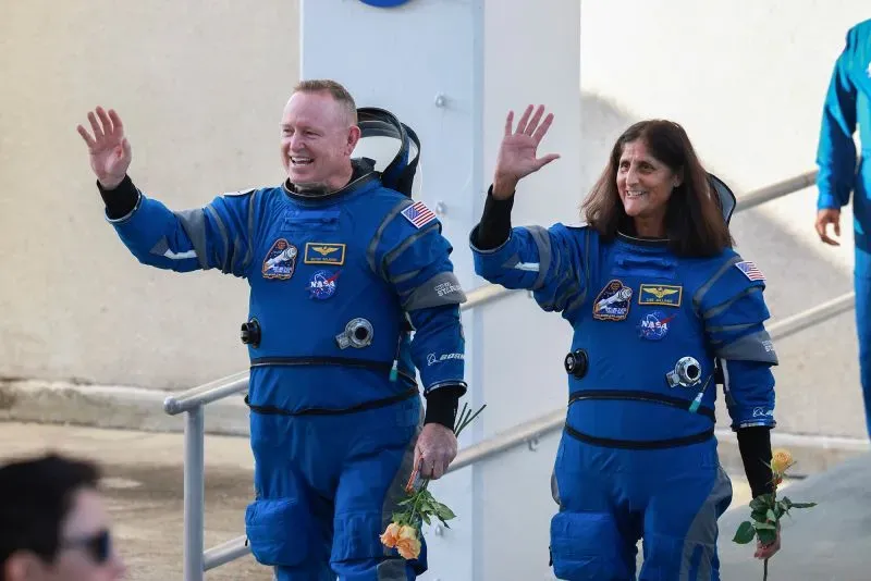 رواد الفضاء سوني ويليامز وبوتش ويلمور يرتديان بدلات الفضاء، يلوحان بيديهما ابتهاجًا أثناء استعدادهم للعودة إلى الأرض بعد مهمة طويلة.