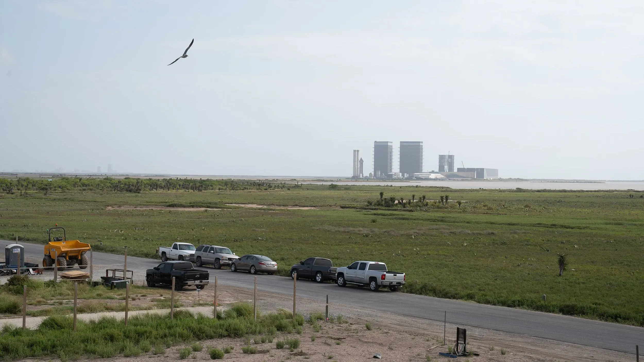 منظر للحرم الجامعي لشركة سبيس إكس في ستاربايس، مع وجود مباني الإطلاق وسيارات على جانب الطريق، محاط بأراضٍ خضراء واسعة.