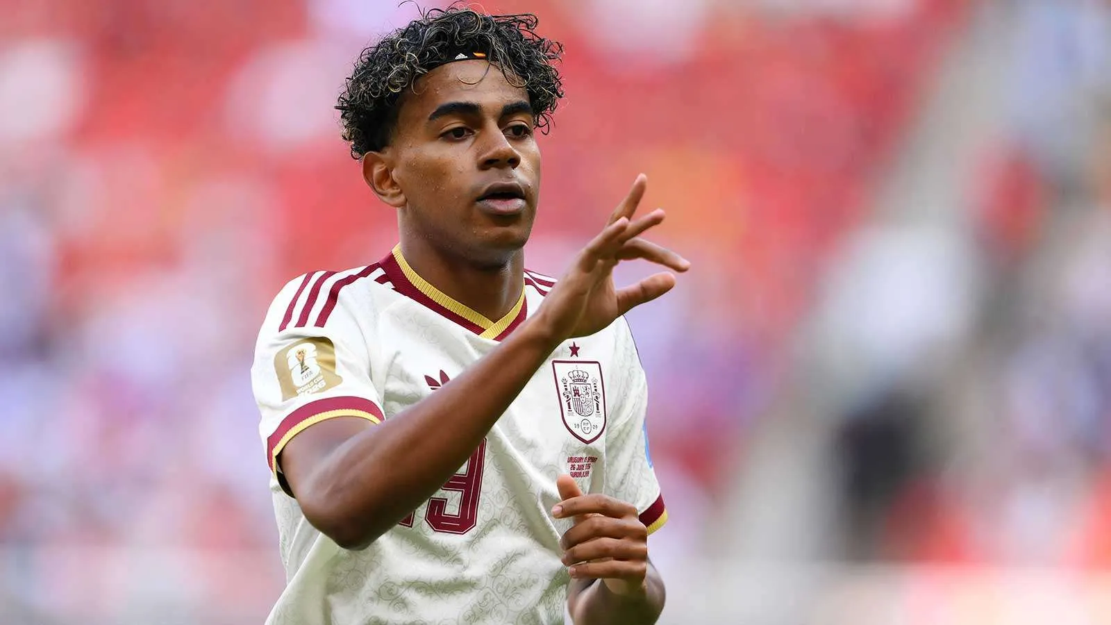 لاعب كرة قدم إسباني شاب يرتدي زي منتخب إسبانيا الأبيض خلال مباراة، مع تركيز على طموحه وجدارته بجائزة الكرة الذهبية.