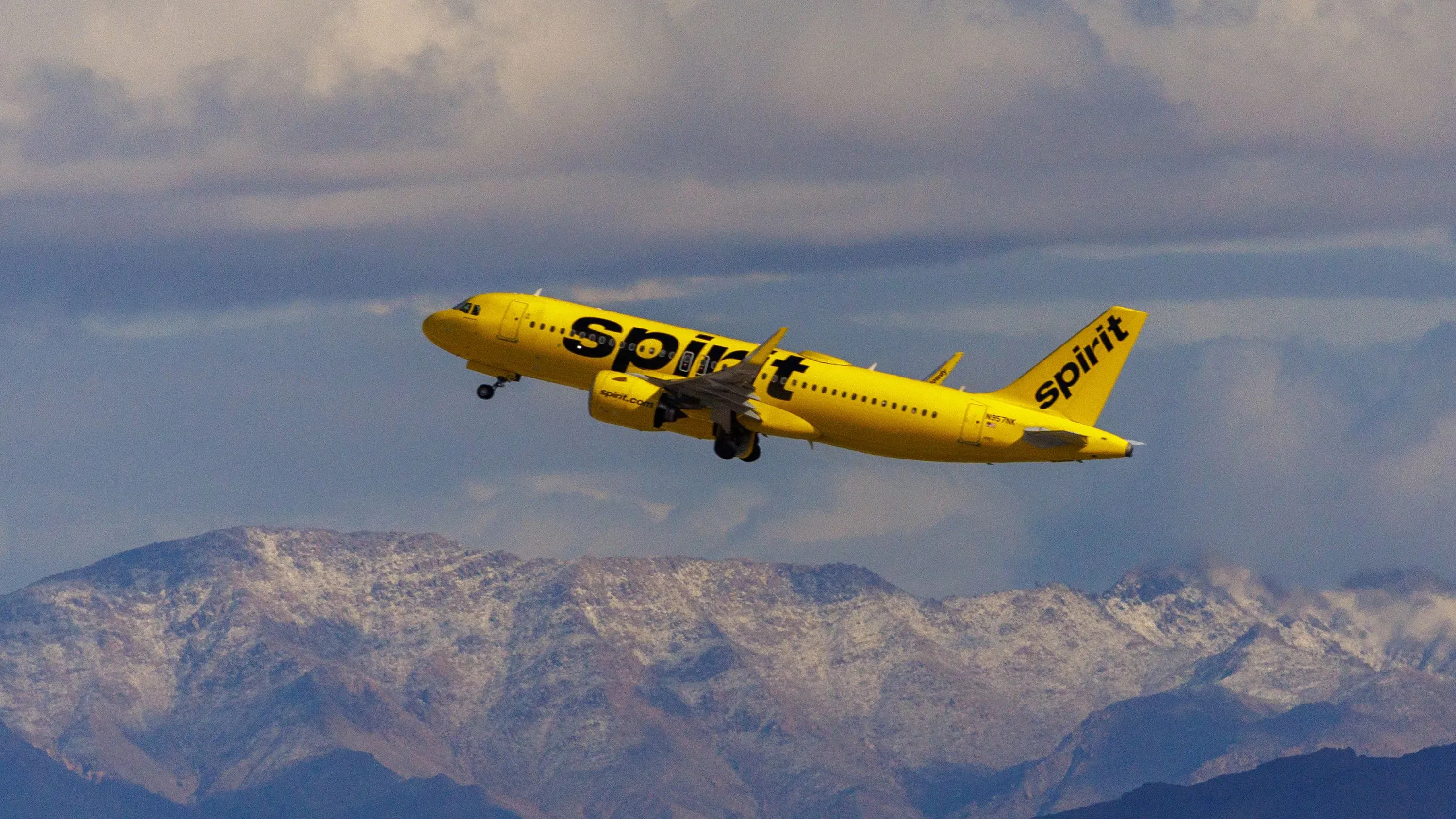طائرة Spirit Airlines الصفراء تحلق فوق جبال مغطاة بالثلوج، تعبيرًا عن إعادة هيكلة ديون الشركة والخروج من الإفلاس.