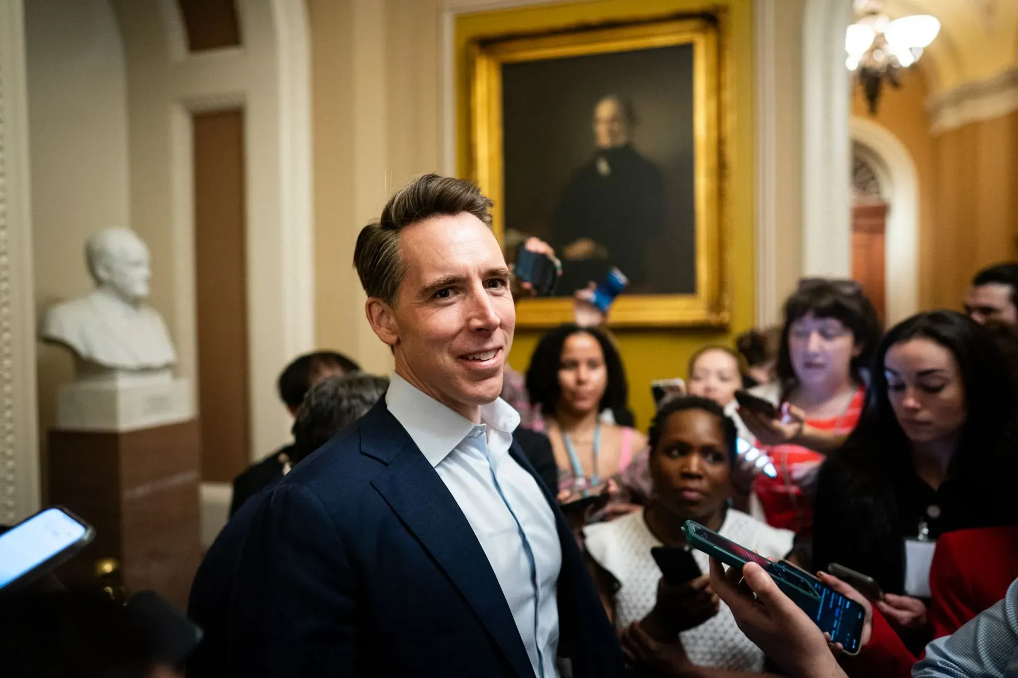 رجل يتحدث مع مجموعة من الصحفيين في قاعة الكونغرس، مع وجود تمثال في الخلفية، في سياق النقاش حول قضايا العمل والنقابات.