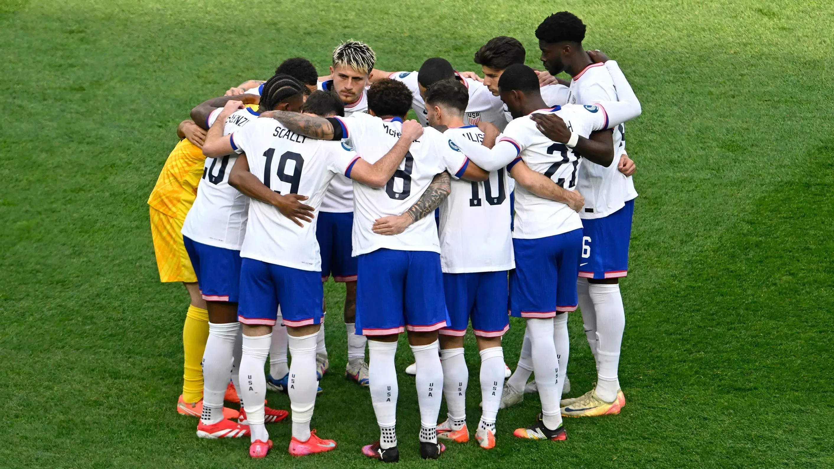 فريق منتخب الولايات المتحدة للرجال يتجمع في دائرة استعدادًا للمباراة، مع التركيز على التعاون والتضامن قبل المنافسة.