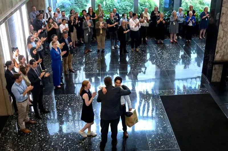 موظفو وزارة الخارجية يودعون زميلًا في حفل مؤثر، وسط تصفيق الحضور في قاعة حديثة، مما يعكس تأثير التخفيضات الأخيرة على الفريق.