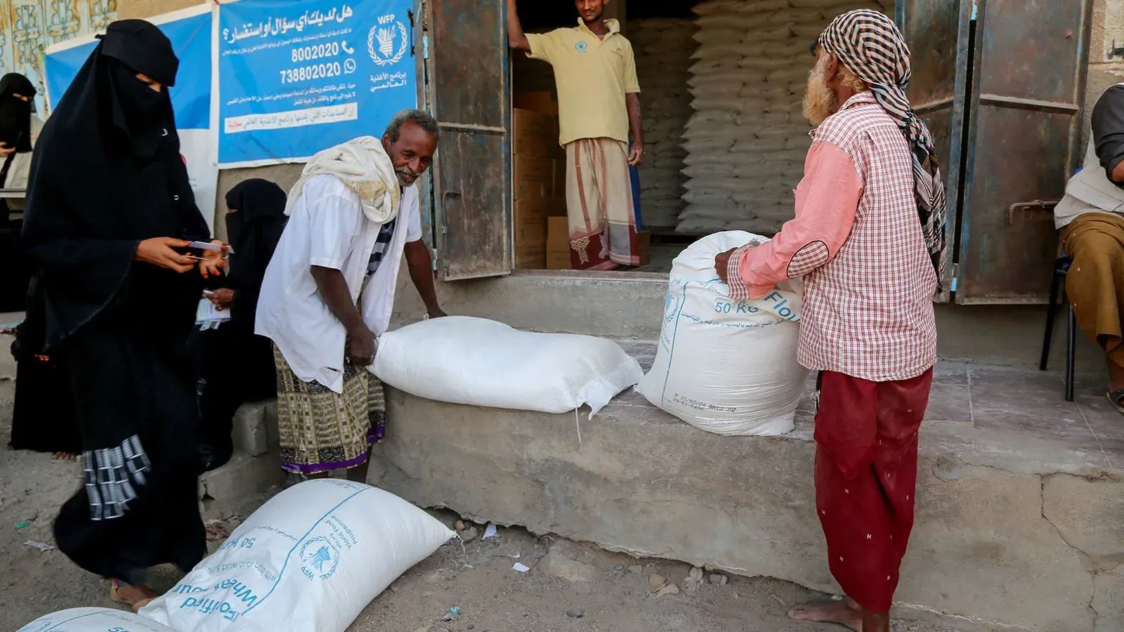 مواطنون يمنيون يستلمون أكياس القمح من مركز توزيع تابع لبرنامج الأغذية العالمي، في ظل أزمة إنسانية متفاقمة.