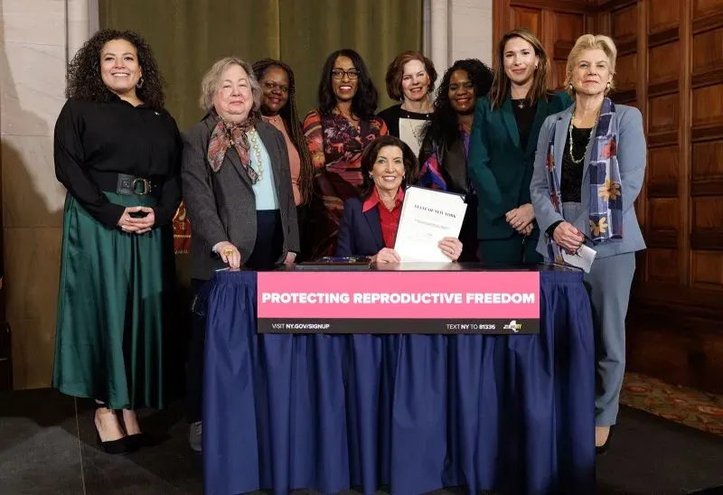 مجموعة من النساء يجلسن ويقفن حول طاولة، حيث تضع إحداهن توقيعها على وثيقة تتعلق بحماية حقوق الإنجاب.