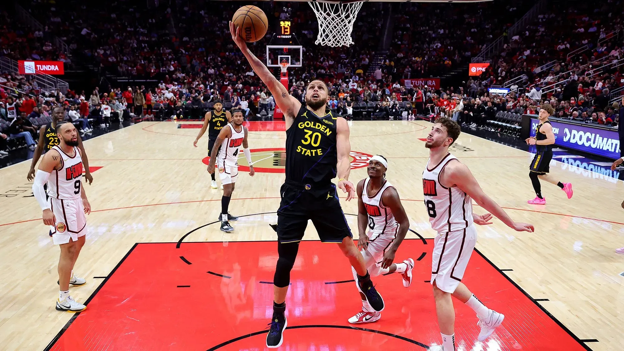 ستيف كاري، لاعب غولدن ستيت ووريورز، يسجل نقطة في مباراة كرة سلة، مع وجود لاعبين من الفريق المنافس في الخلفية.