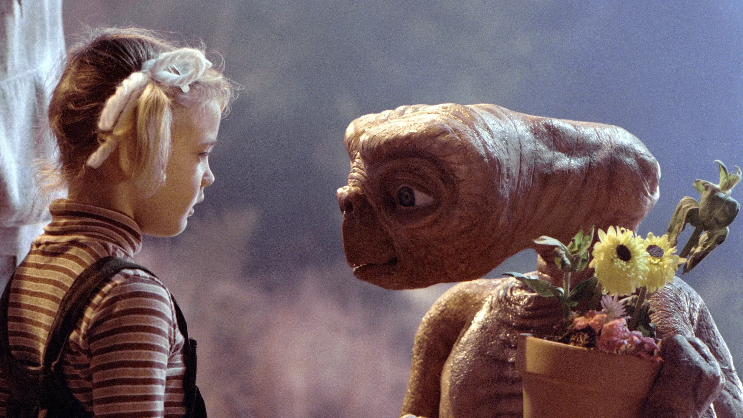 مشهد شهير من فيلم "E.T. the Extra-Terrestrial" يظهر طفلة تواجه الكائن الفضائي E.T. وهو يحمل زهورًا، مع تفاعل مليء بالبراءة والدهشة.