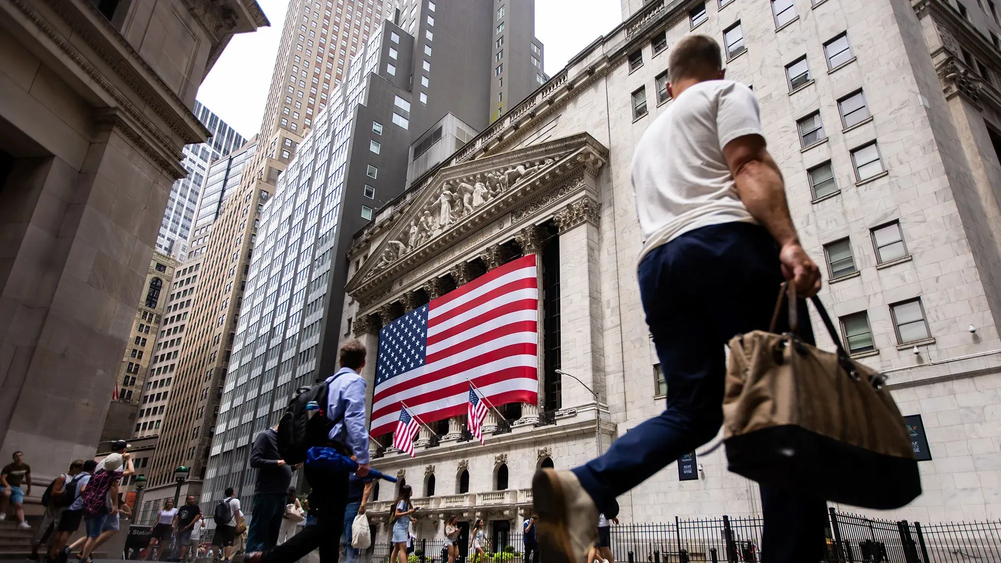 مارة أمام بورصة نيويورك مع العلم الأمريكي يتدلى من المبنى، في سياق ترقب الأسواق لإعلانات ترامب عن التعريفات الجمركية.