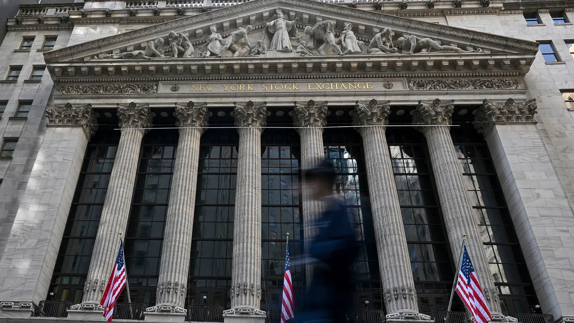 واجهة بورصة نيويورك مع أعمدة ضخمة وأعلام أمريكية، تعكس التوترات الاقتصادية بعد انتقادات ترامب لرئيس الاحتياطي الفيدرالي.