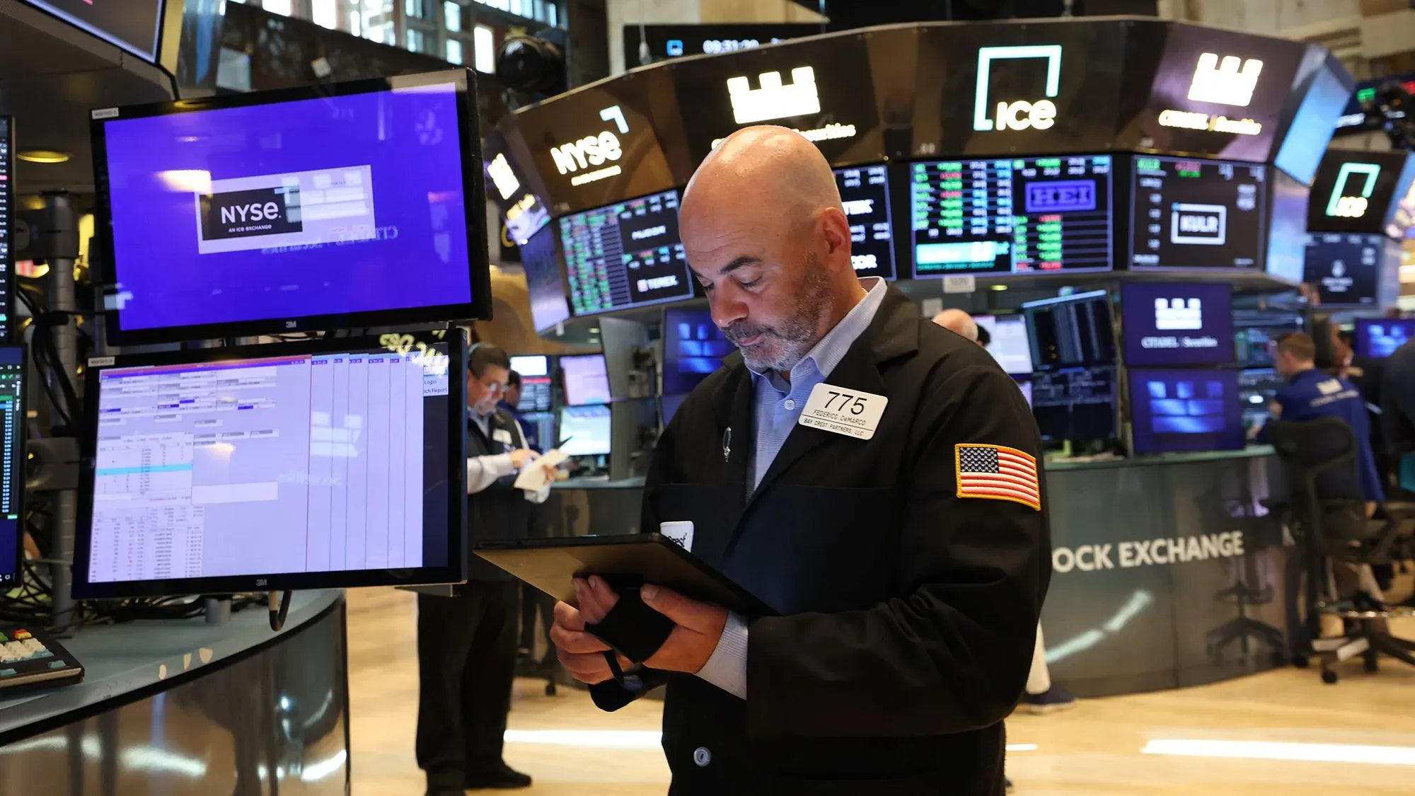 متداول في بورصة نيويورك يستخدم جهاز لوحي، محاط بشاشات تعرض بيانات السوق، في ظل تأثيرات حكم المحكمة على العقود الآجلة للأسهم.