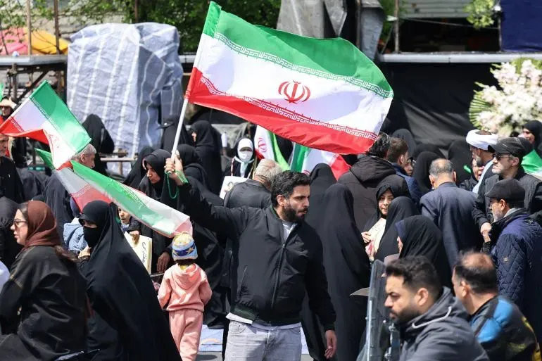 محتجون إيرانيون يحملون الأعلام الوطنية في تجمع حاشد، مع التركيز على الأجواء السياسية المتوترة في المنطقة.