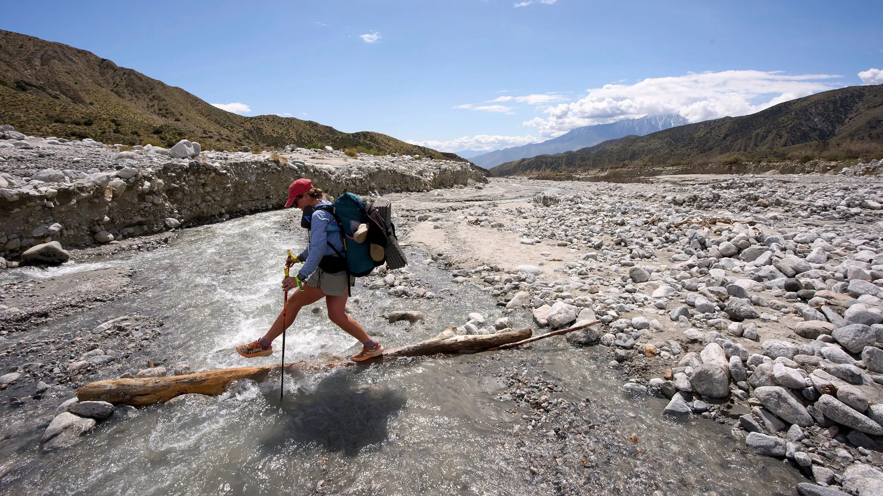 مغامر يتنزه عبر مجرى مائي ضيق على مسار باسيفيك كريست، محاط بتضاريس جبلية وصخور، مما يعكس تحديات التنزه في الطبيعة.