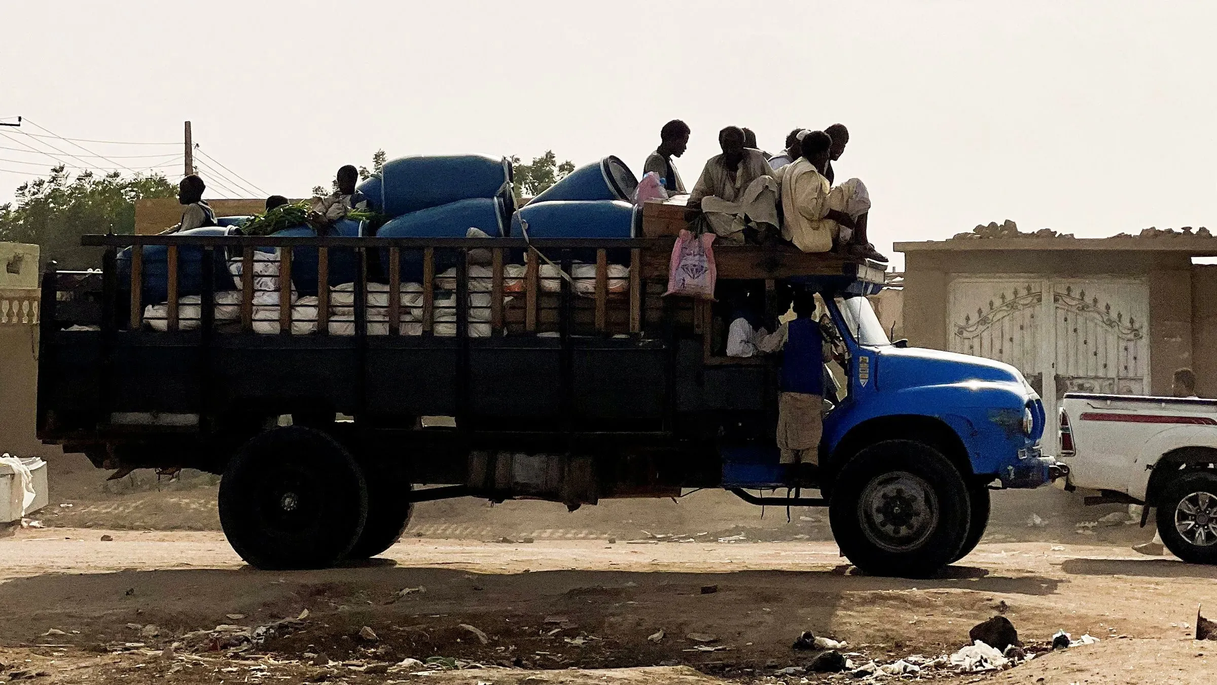 شاحنة زرقاء محملة بالسلع، يجلس عليها عدد من الأشخاص في منطقة ريفية بالسودان، تعكس آثار النزاع المستمر في البلاد.