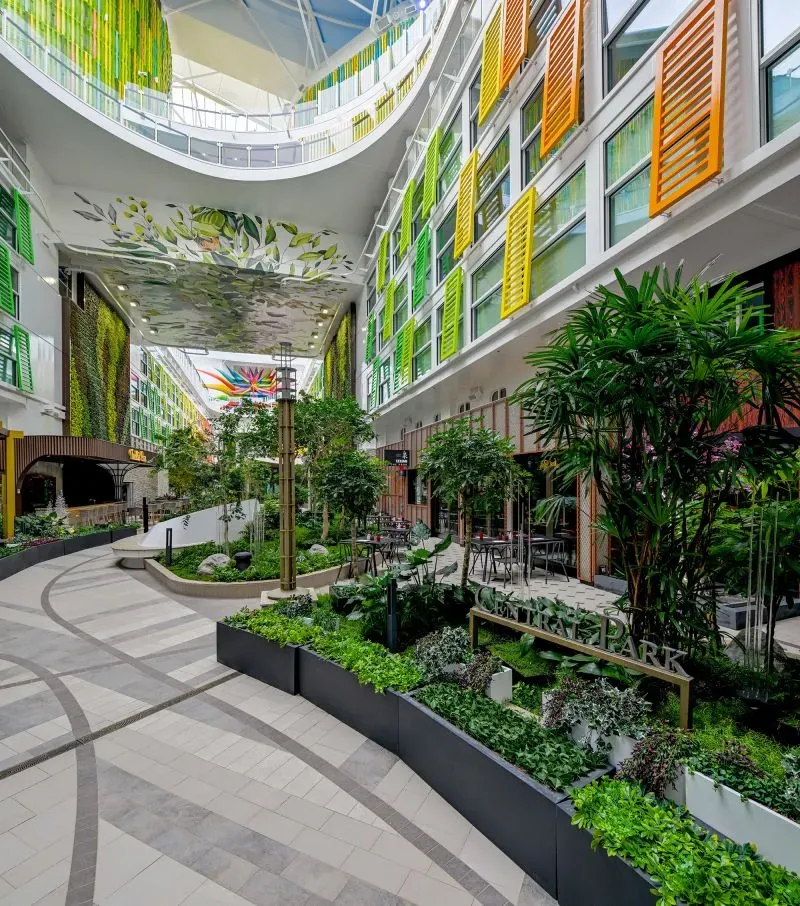 منطقة خضراء داخلية في سفينة سياحية حديثة، تحتوي على نباتات وصناديق زهور، مع تصميم عصري وألوان زاهية، تعكس تجربة فاخرة للركاب.