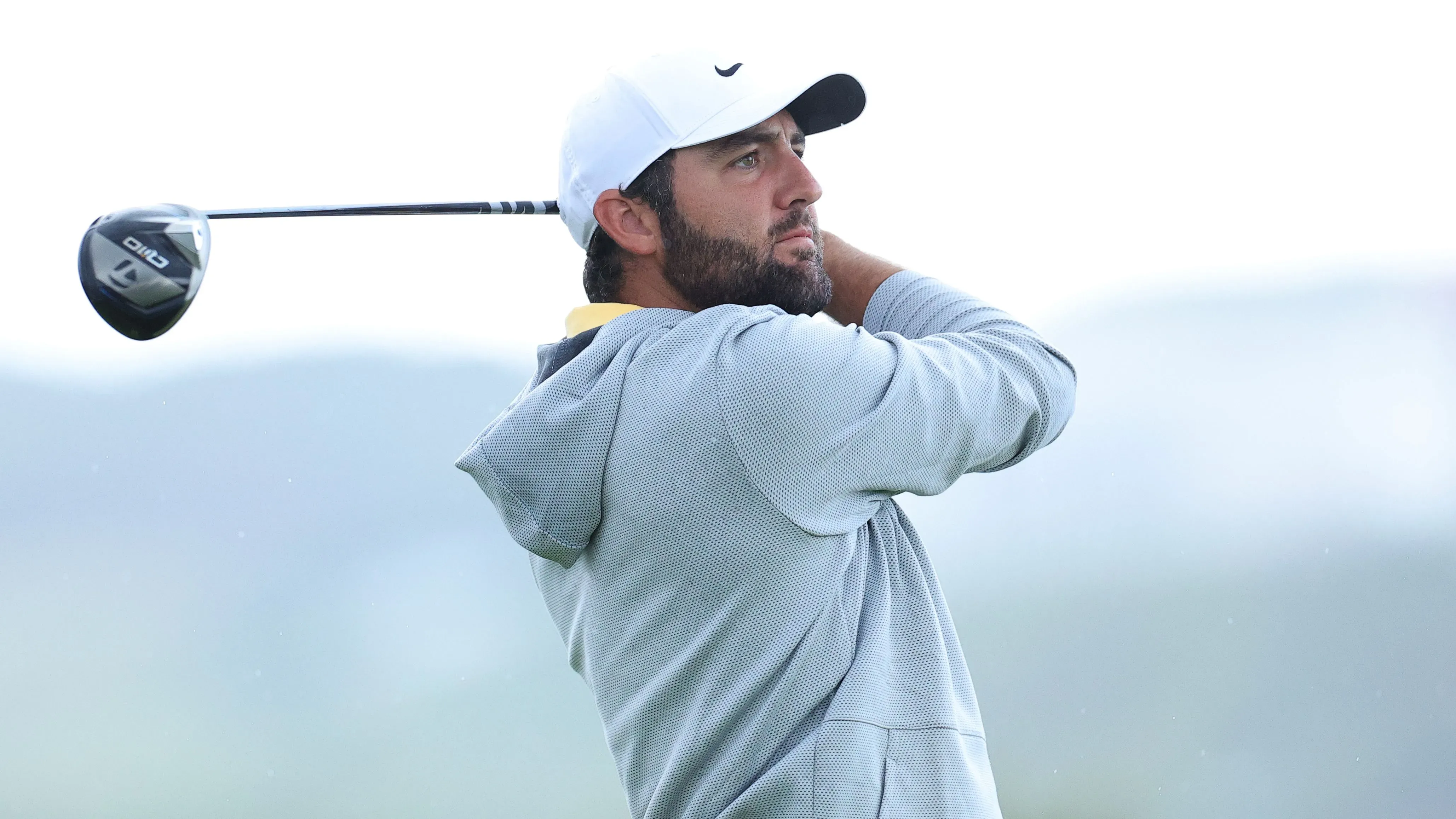 لاعب الغولف براين هارمان أثناء تسديد ضربة، يظهر التركيز في وجهه وسط أجواء غائمة، مع وجود منظر طبيعي في الخلفية.