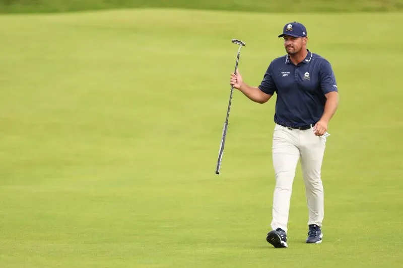 لاعب الجولف براين هارمان يمشي على الملعب حاملاً عصا الجولف، مع التركيز على أدائه القوي في البطولة المفتوحة.