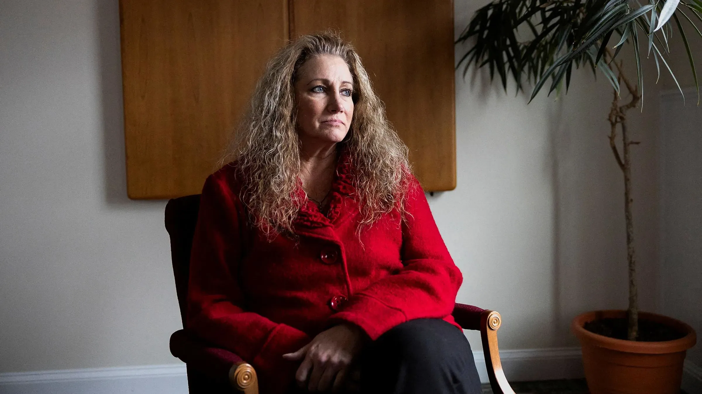 امرأة تجلس في غرفة مضاءة بشكل خافت، ترتدي سترة حمراء، تعبر عن مشاعر القلق أو التأمل، في سياق قضية قانونية حول التمييز في العمل.