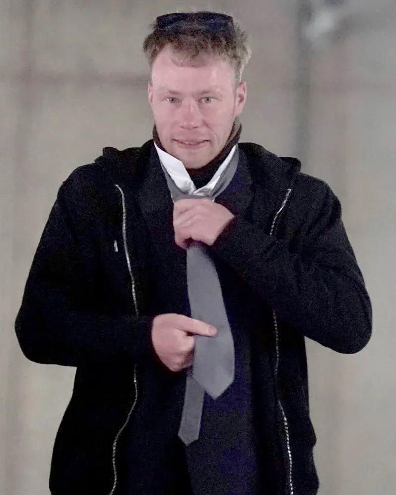 رجل يرتدي ملابس داكنة ويقوم بربط ربطة عنق، يظهر في خلفية محكمة بعد إدانته بتهمة الإضرار بشجرة تاريخية وسور هادريان.