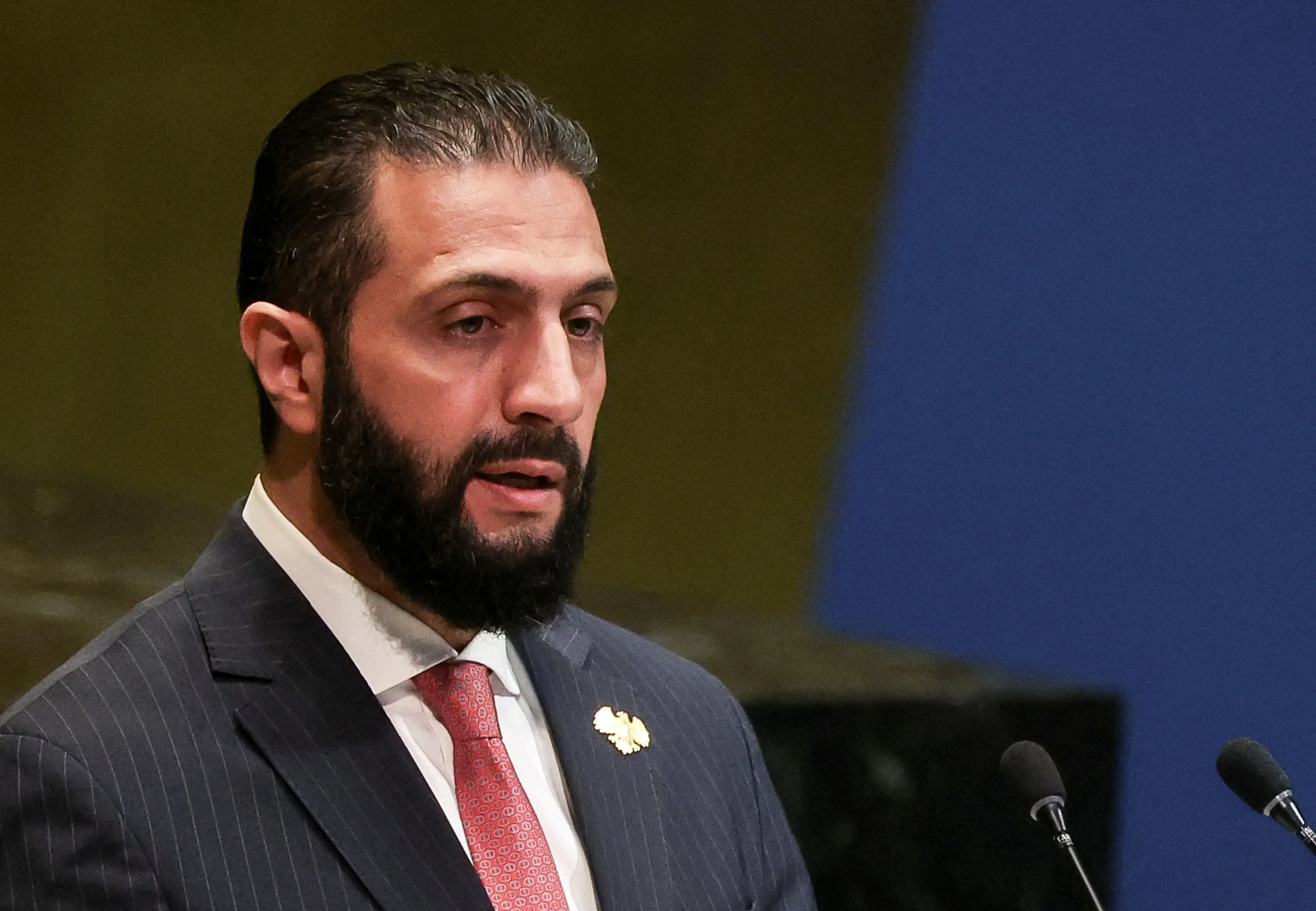 رجل يتحدث في مؤتمر، يعبر عن أهمية الانتخابات البرلمانية في سوريا كخطوة نحو الانتقال السياسي بعد الحرب.