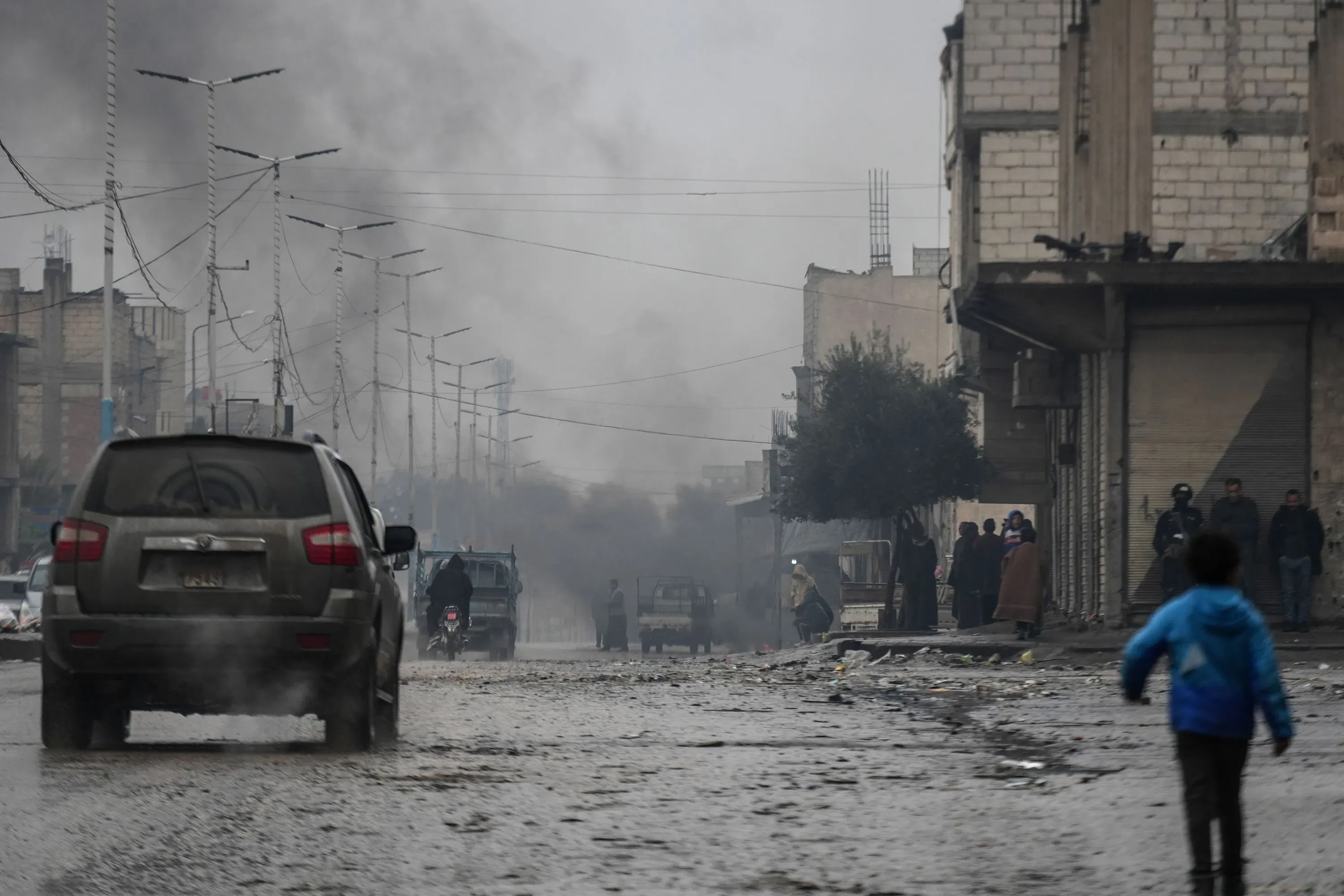 مدينة الرقة السورية بعد استعادة الجيش السوري السيطرة عليها، تظهر سيارات في الشارع مع دخان في الخلفية، مما يعكس الوضع الأمني المتوتر.