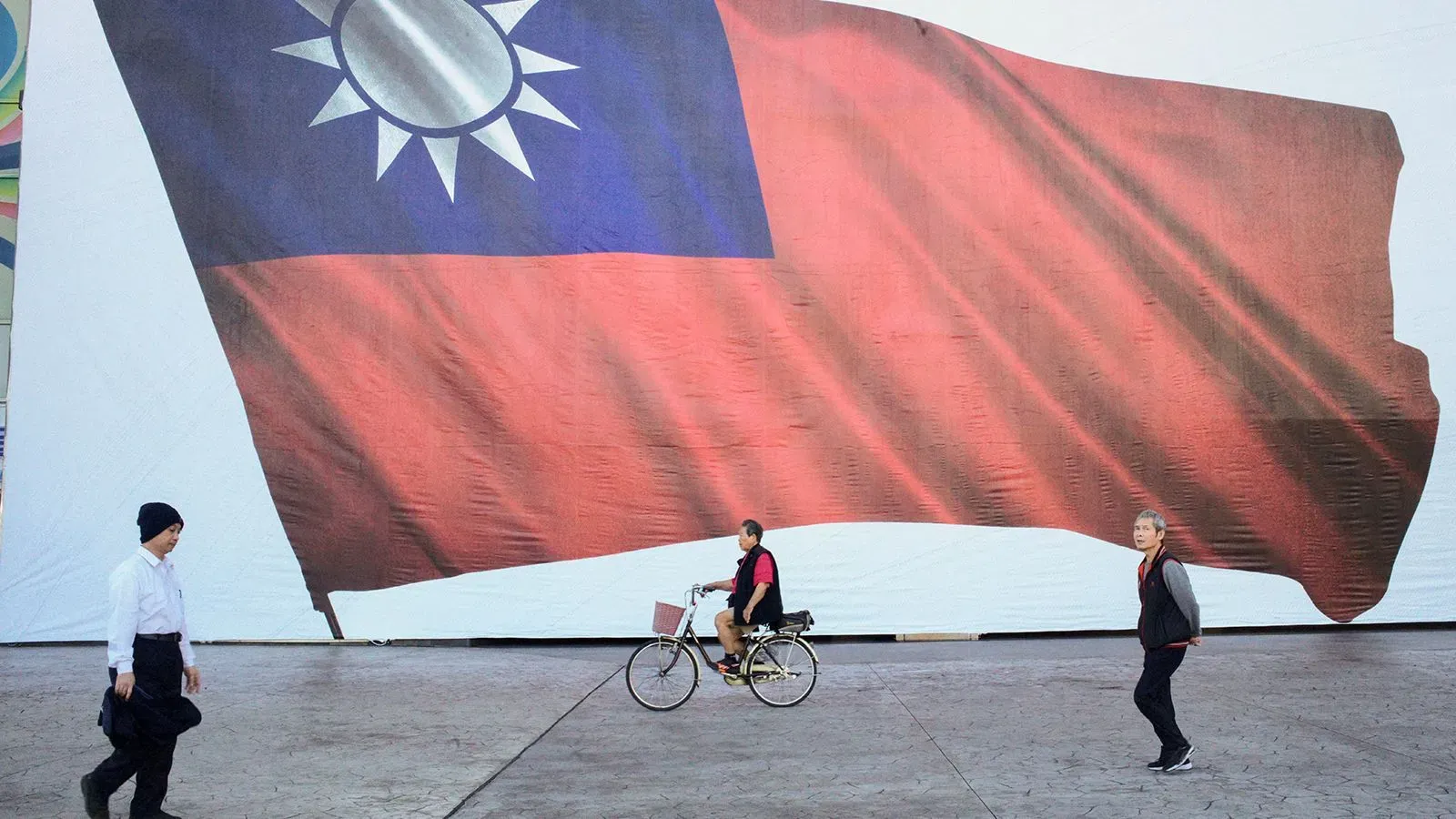 رجل يقود دراجة أمام علم تايواني كبير، يعكس تصاعد التوترات بين تايوان والصين وسط قضايا التجسس المتزايدة.