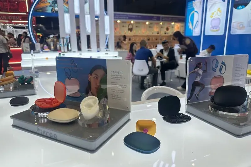 عرض لمجموعة من المنتجات الإلكترونية الحديثة في معرض تجاري في هونغ كونغ، مع وجود زوار يتفاعلون في الخلفية.