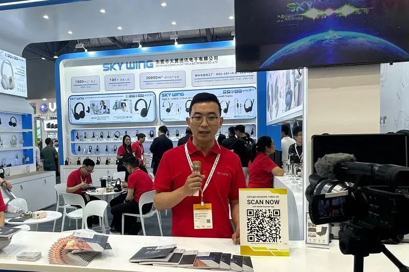 رجل يتحدث في معرض Sky Wing للالكترونيات، محاط بمنتجات صوتية وعروض، حيث يتناول تأثير الحرب التجارية على الصناعة.