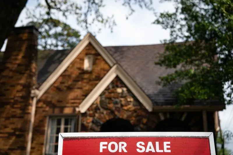 لافتة "للبيع" أمام منزل تقليدي، تشير إلى حالة سوق العقارات المتقلبة وتأثير الاقتصاد على قرارات الشراء.