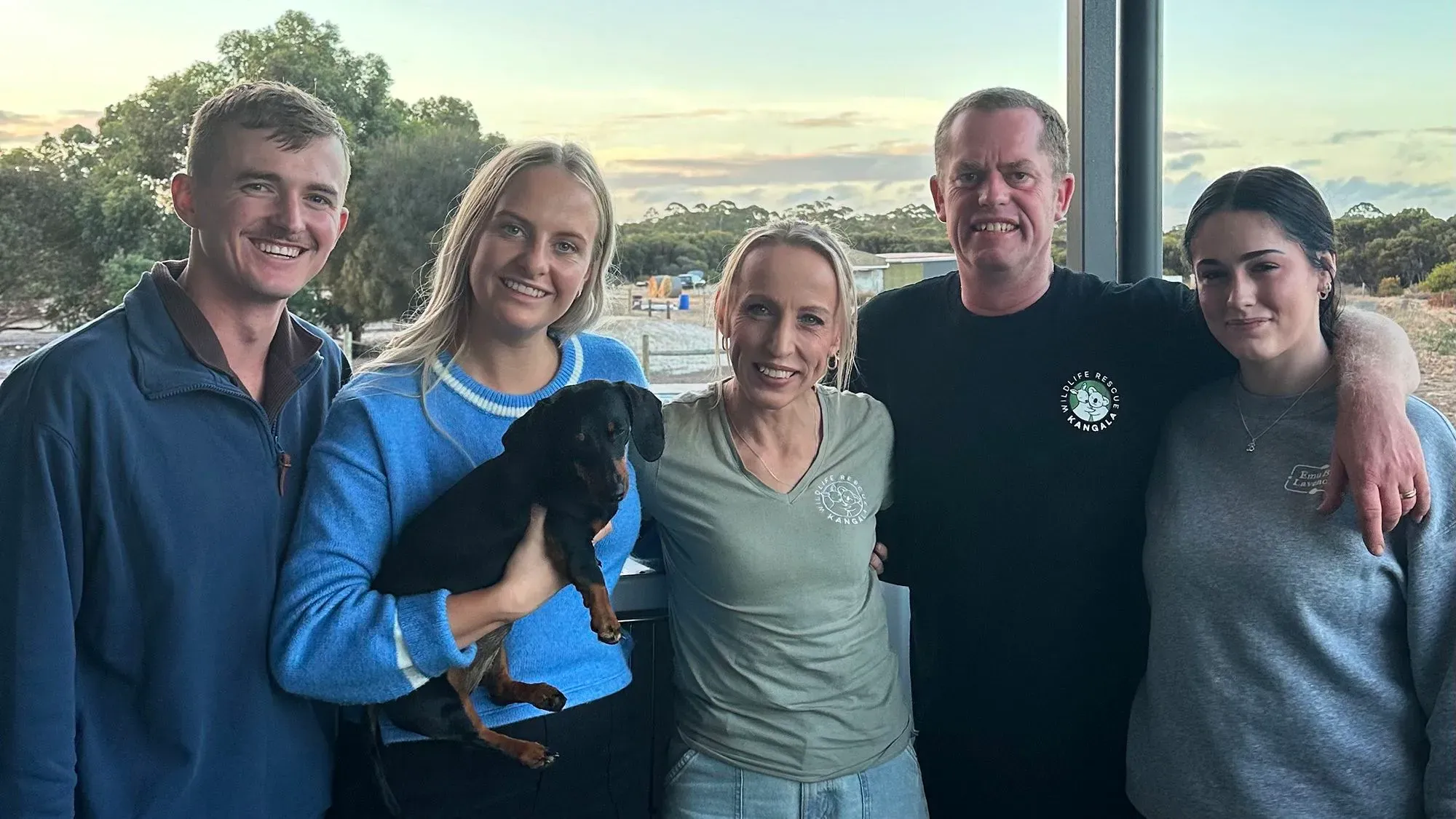 فاليري، الكلبة الألمانية، تُحمل بين ذراعي مالكيها بعد لم شملها بعد 540 يوماً في جزيرة الكنغر، مع تعبيرات الفرح والاحتضان.