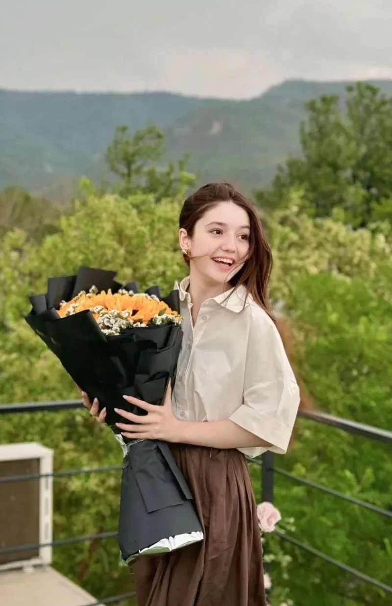 سناء يوسف تحمل باقة من الزهور وتبتسم في أجواء طبيعية، تعكس فرحتها بعيد ميلادها قبل أيام من مأساتها.