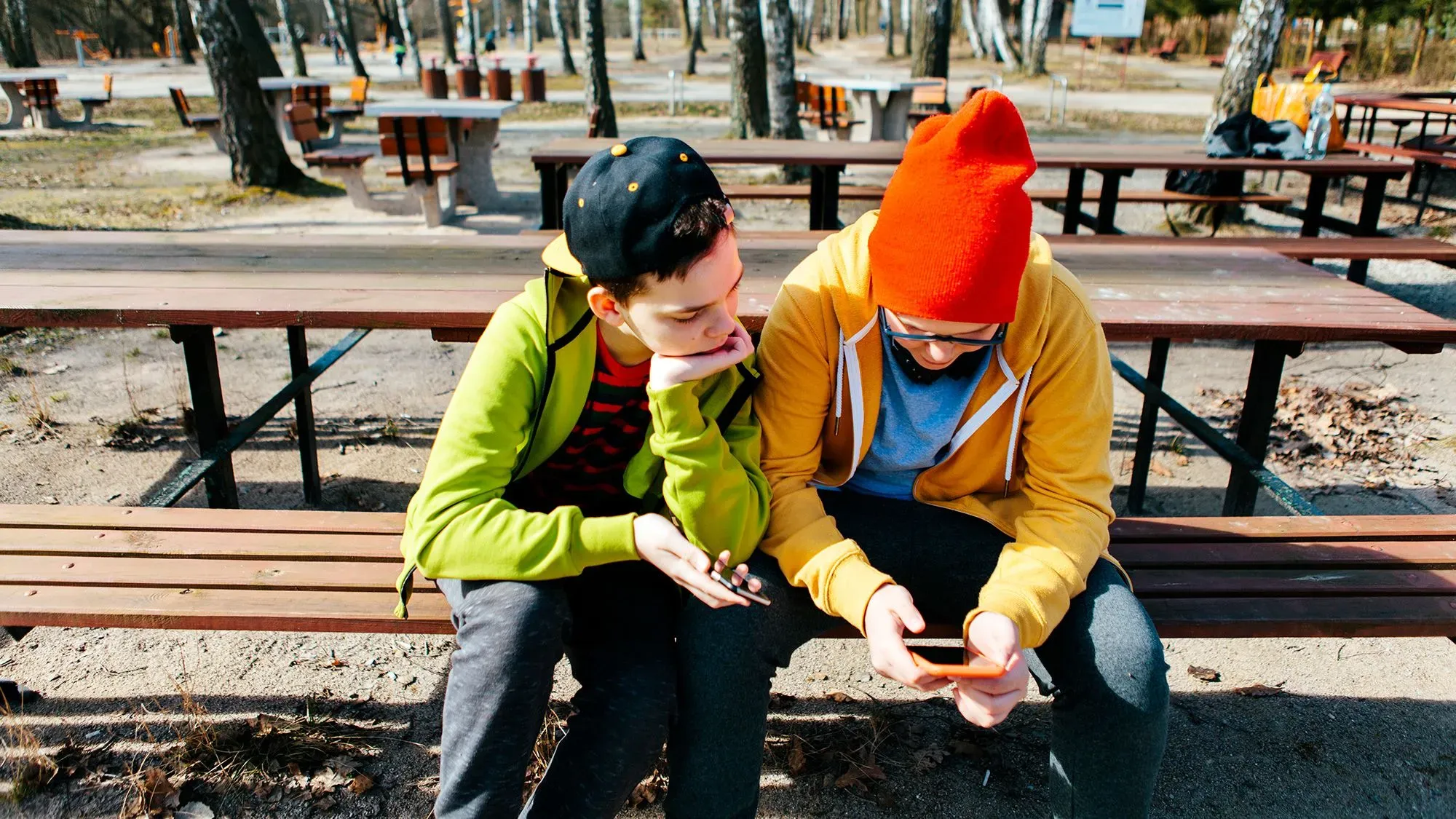 شخصان يجلسان على مقعد في حديقة، يتابعان محتوى على الهاتف. يعبران عن اهتمام وهما يستعرضان فيديو مثير.