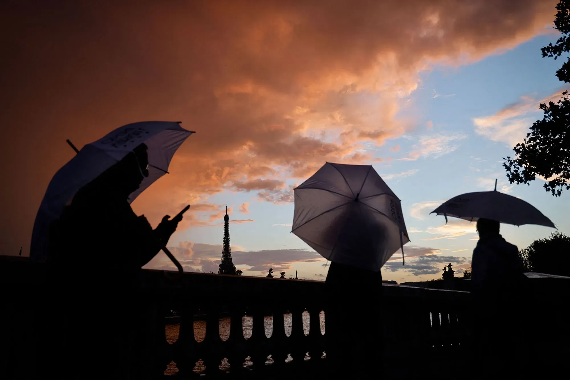 أشخاص يحملون مظلات في غروب الشمس، مع معالم بارزة مثل برج إيفل في الخلفية، مما يعكس جمال الحياة في الخارج.