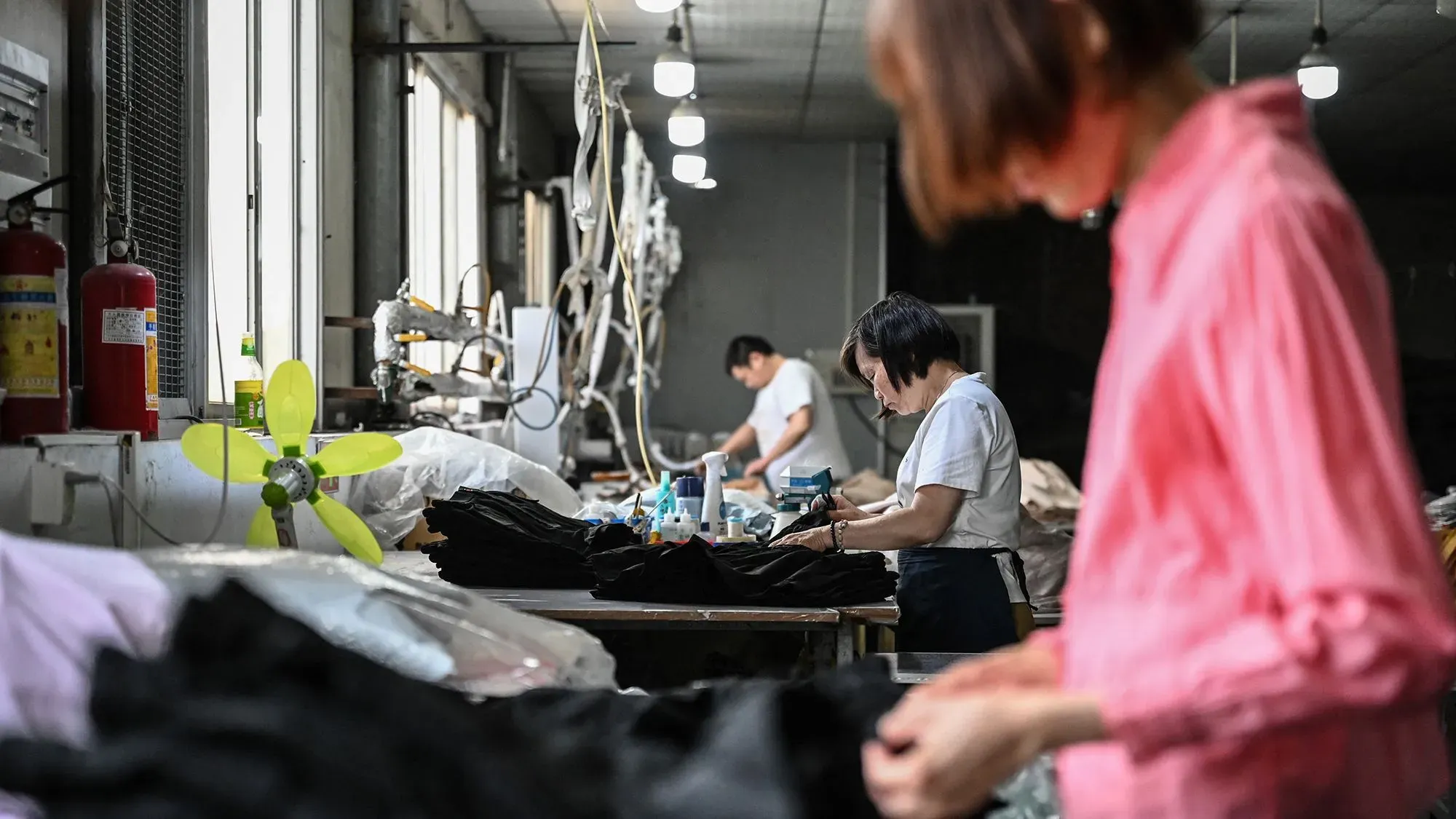 عمال في مصنع ملابس يعملون على تجهيز المنتجات، مع وجود أدوات وخامات حولهم، مما يعكس عملية الإنتاج في التجارة الإلكترونية.