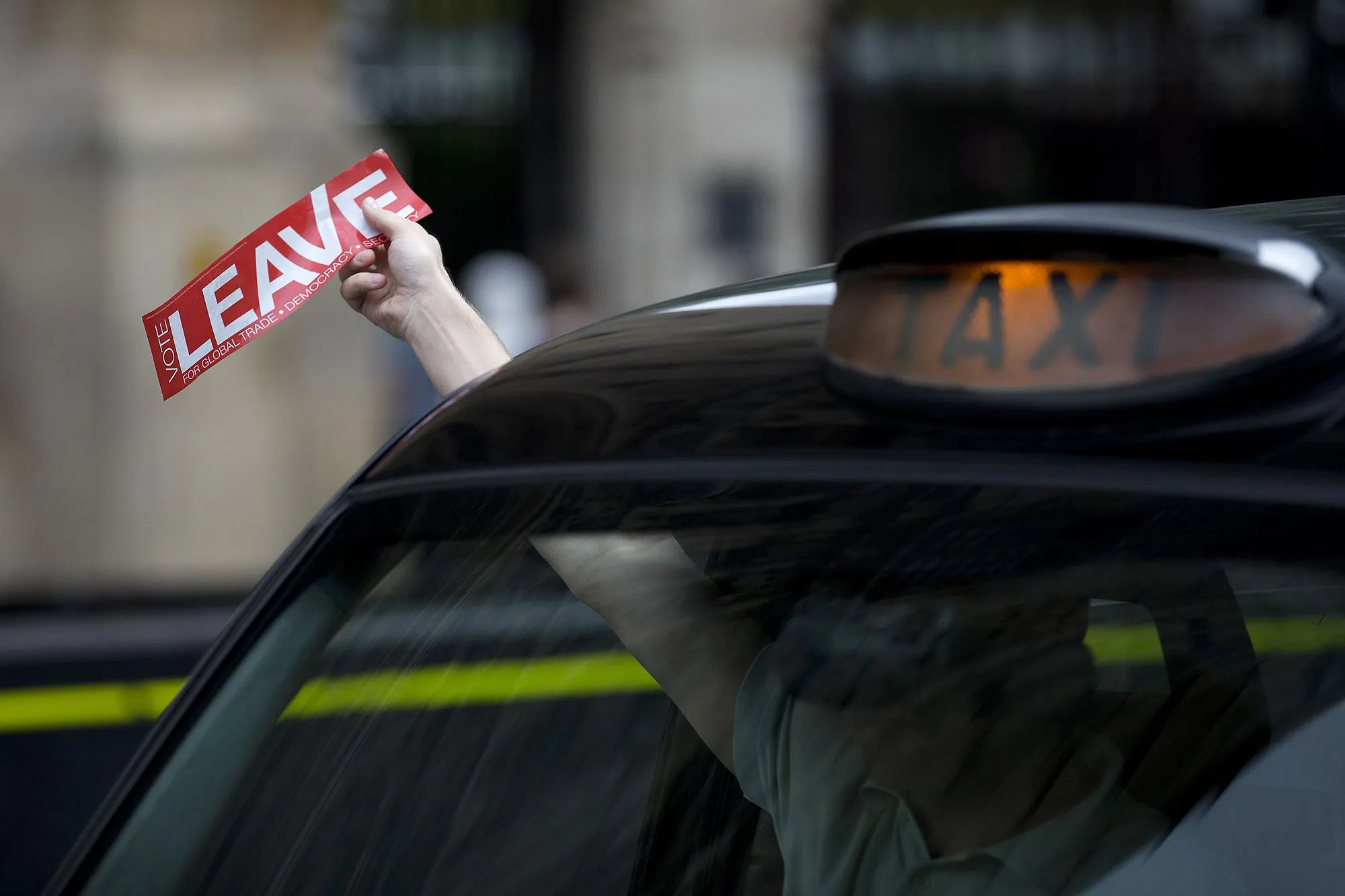 يد تظهر يد ترفع لافتة حمراء مكتوب عليها "LEAVE" من نافذة سيارة أجرة، تعبيراً عن دعم الخروج من الاتحاد الأوروبي.