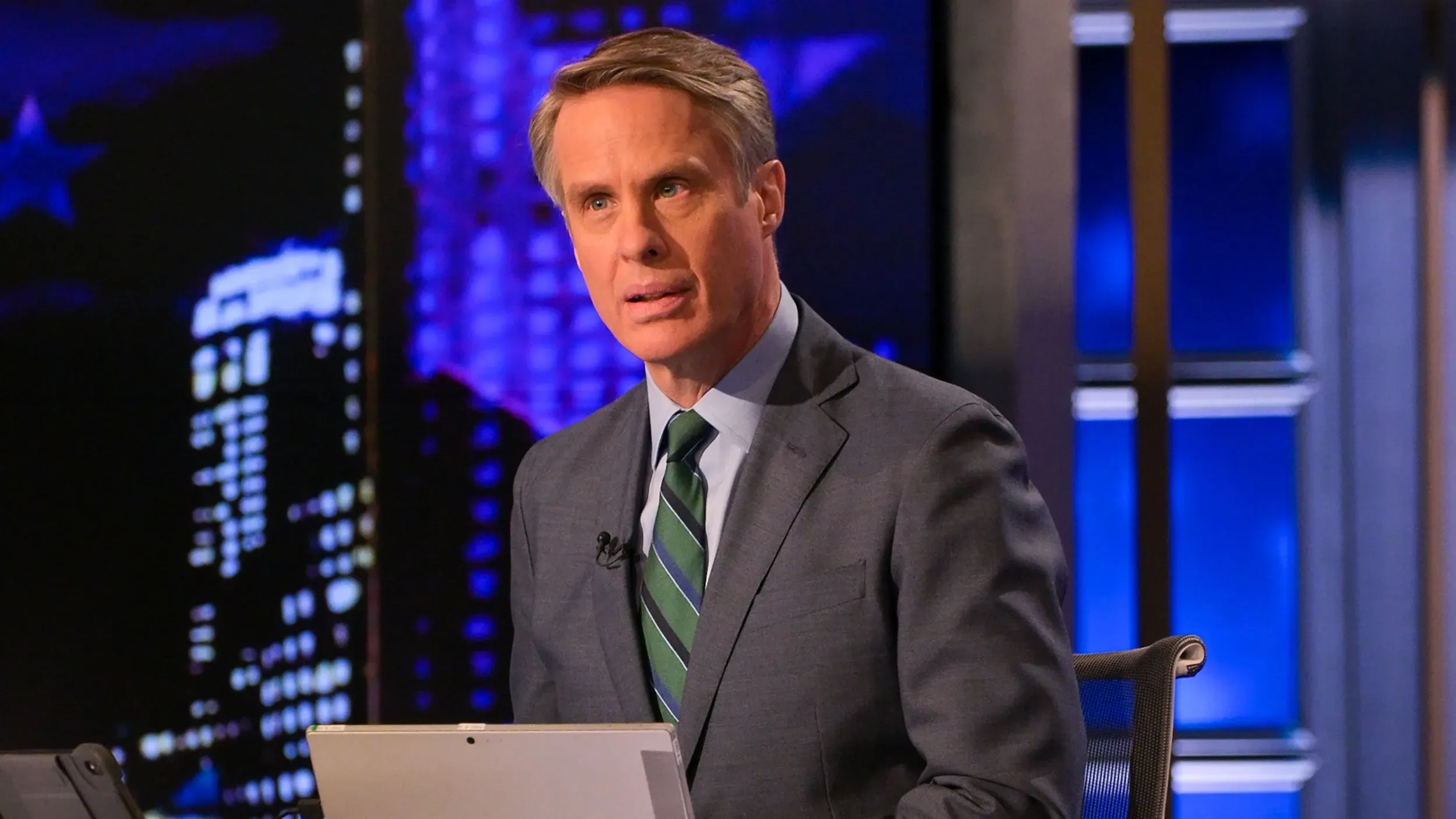 تيري موران يتحدث بجدية أثناء تقديمه برنامجًا إخباريًا، مع خلفية مضاءة تعكس أجواء استوديو التلفزيون.