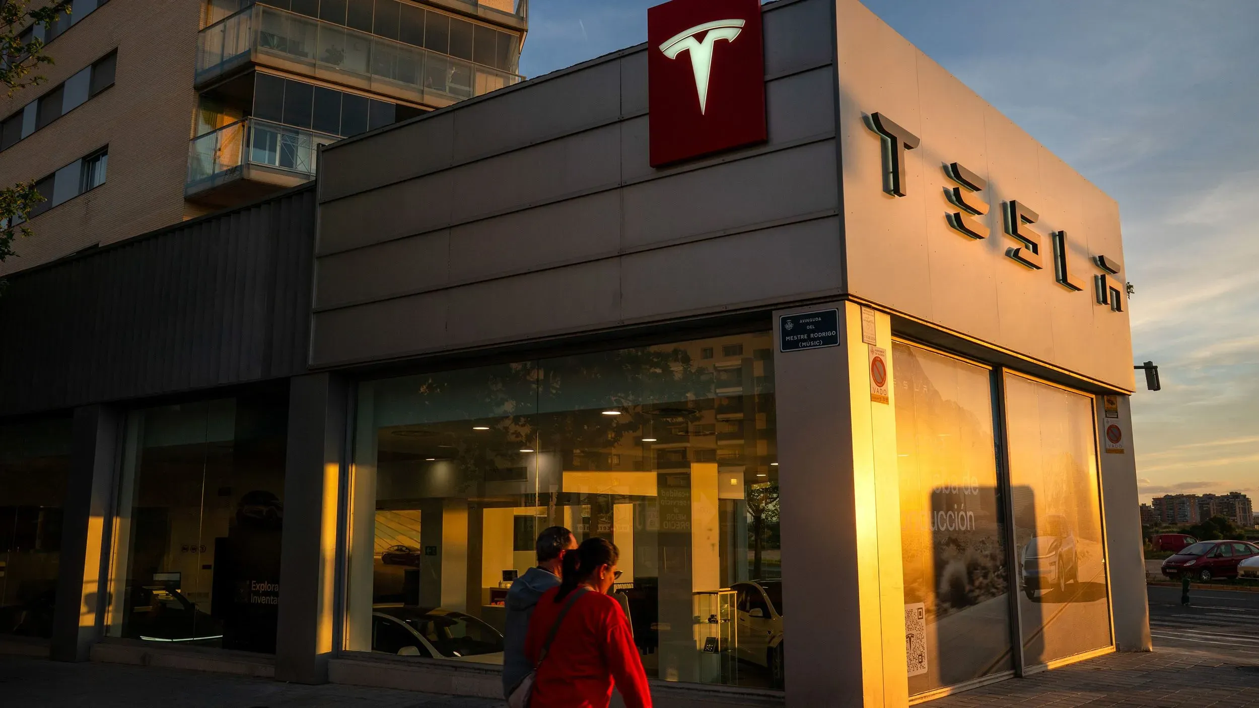 تظهر الصورة واجهة متجر تسلا مع لافتة الشركة، حيث يتجول زبائن في المساء، مما يعكس تراجع مبيعات تسلا في أوروبا.